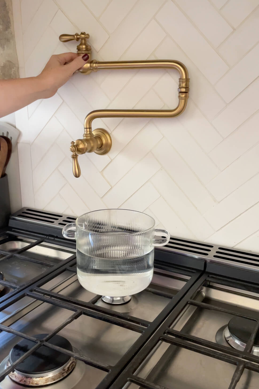 Hand turning on a brass pot filler above a glass pot of water on a stove.